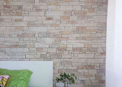 Interiér cihlového bytu, ložnice, kamenný obklad, postel, noční stolky