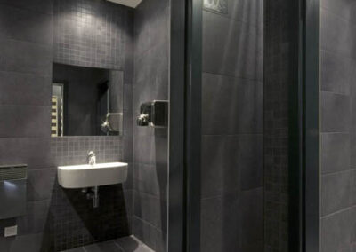 Interiér baru v Poděbradech, toalety, WC, tmavý obklad, šedá dlažba, bílé umyvadlo, zrcadlo