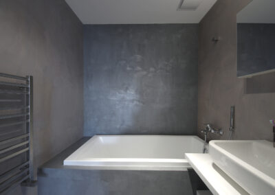 Byt v novostavbě, koupelna, betonová stěrka, vana, umyvadlo, nástěnné zrcadlo, police pod umyvadlem