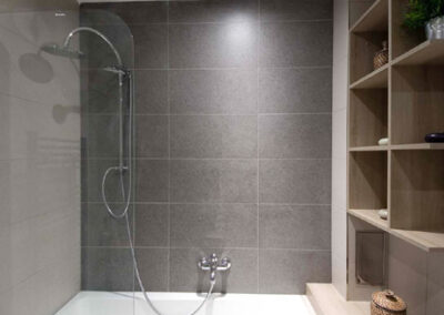 Interiér cihlového bytu, koupelna, radiátor, vana, sprchová zástěna, sprchový sloup, police v koupelně