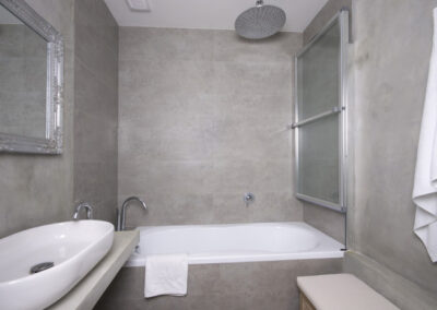 Interiér bytu Řešovská, panelákový byt, kompletní rekonstrukce, koupelna, šedý obklad, šedá cementová stěrka, umyvadlo na desce, vana, sprchová zástěna na vaně, zrcadlo ve stříbrném rámu