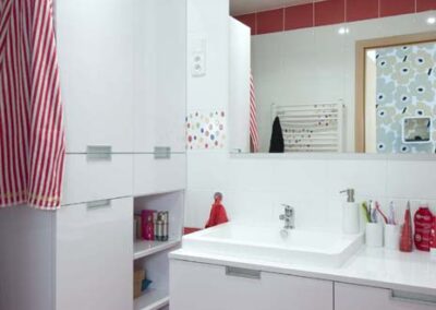 Interiér panelákového bytu, koupelna, bílý a červený obklad, umyvadlo, zrcadlo, skříň v koupelně