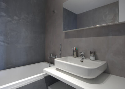 Byt v novostavbě, koupelna, betonová stěrka, vana, umyvadlo, nástěnné zrcadlo, police pod umyvadlem