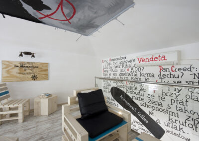 Interiér kavárny AnonymouS, grafika na zdi, dřevěný nábytek, modré pruhy, malba na stropě, sezení na dřevěném nábytku