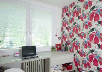 Interiér panelákového bytu, pokoj pro slečnu, pohled na okno, pracovní stůl pod oknem, červeno bílá tapeta