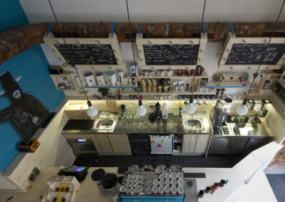 Interiér kavárny AnonymouS, grafika na zdi, dřevěný nábytek, modré pruhy, dřevěný bar, modrá zeď, umělecká malba, kávovar, hrnky, vše na přípravu kávy