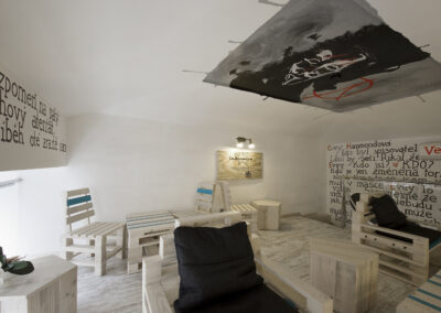 Interiér kavárny AnonymouS, grafika na zdi, dřevěný nábytek, modré pruhy, malba na stropě, sezení na dřevěném nábytku