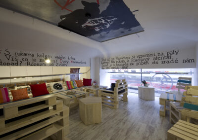 Interiér kavárny AnonymouS, grafika na zdi, dřevěný nábytek, modré pruhy, malba na stropě, sezení na dřevěném nábytku, europalety